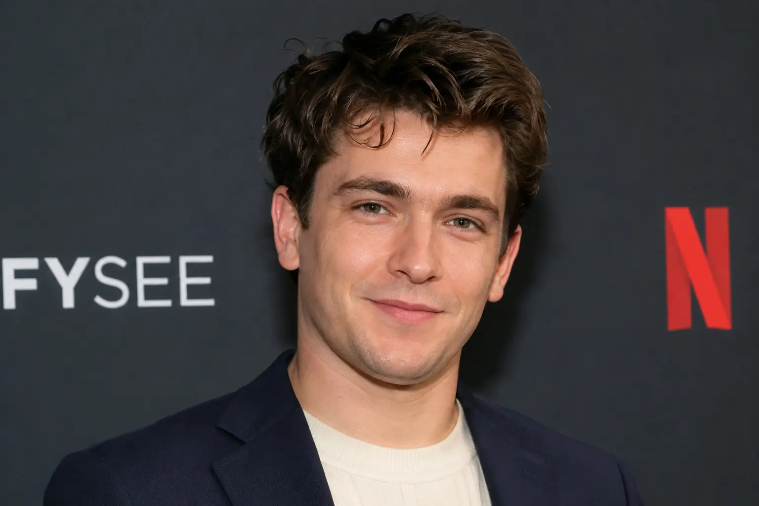 Jake Reiner movies star Jake Reiner smiling on the red carpet at a Netflix FYSEE event in a navy blazer and cream sweater.